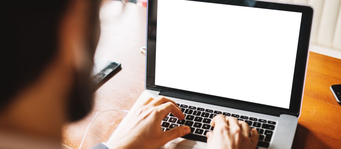 Rear view of young bearded businessman in suit typing on a laptop keyboard at the office. Focus view on a laptop.