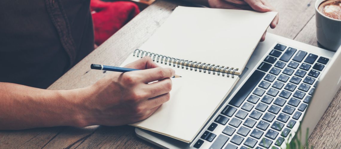 Young business man hand writing notebook and using laptop on woo
