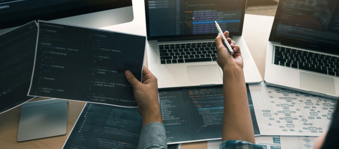 Two software developers are using computers to work together with their partner at the office desk.
